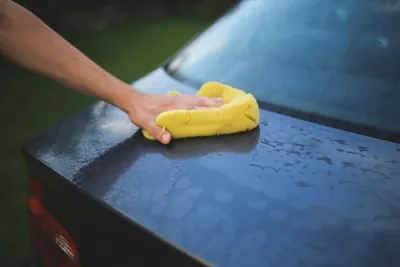 A hand cleaning a blue car with a yellow sponge.