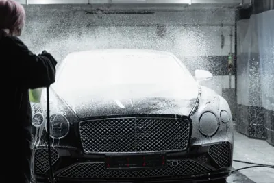 A black luxury car being covered in foam indoors.