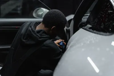 A detailer cleaning inside a car through an open door.