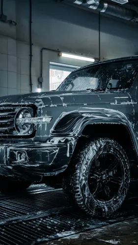 A dark SUV with soap suds in an indoor wash bay.