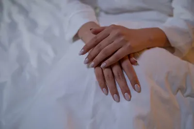 Hands with a soft neutral manicure resting on white fabric.