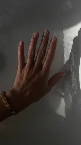 A hand with neutral polished nails and a gold bracelet.