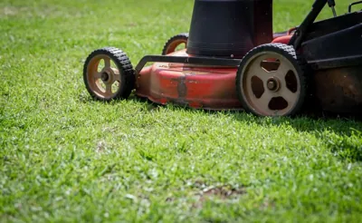 A red lawn mower cutting bright green grass.