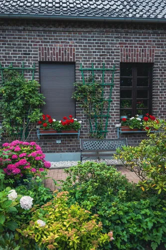 Flowering plants and green shrubs outside a brick house.